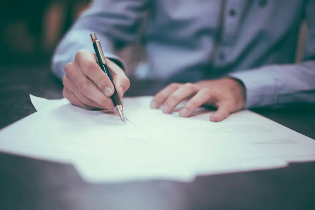 Una persona firma un documento sobre un escritorio. Foto: Unsplash