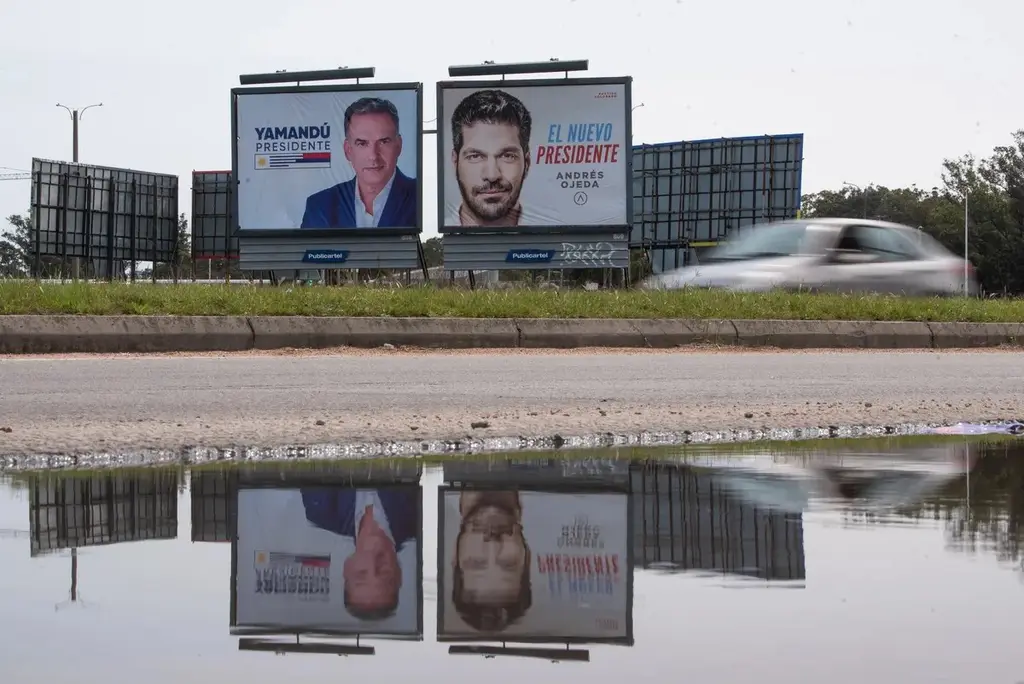 Carteles de campaña de Yamandú Orsi y Andrés Ojeda junto a una ruta, reflejados en un charco, durante la campaña electoral de 2024 (archivo). Foto: Gianni Schiaffarino