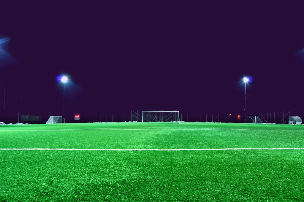 Una cancha de fútbol vacía, de noche, con el arco al fondo y los reflectores encendidos. Foto: Unsplash