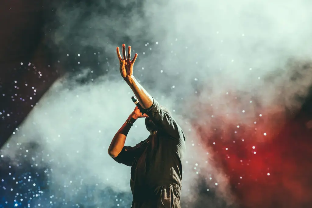 Un cantante de espaldas, con el micrófono y una mano en alto, en un escenario. Foto: Unsplash