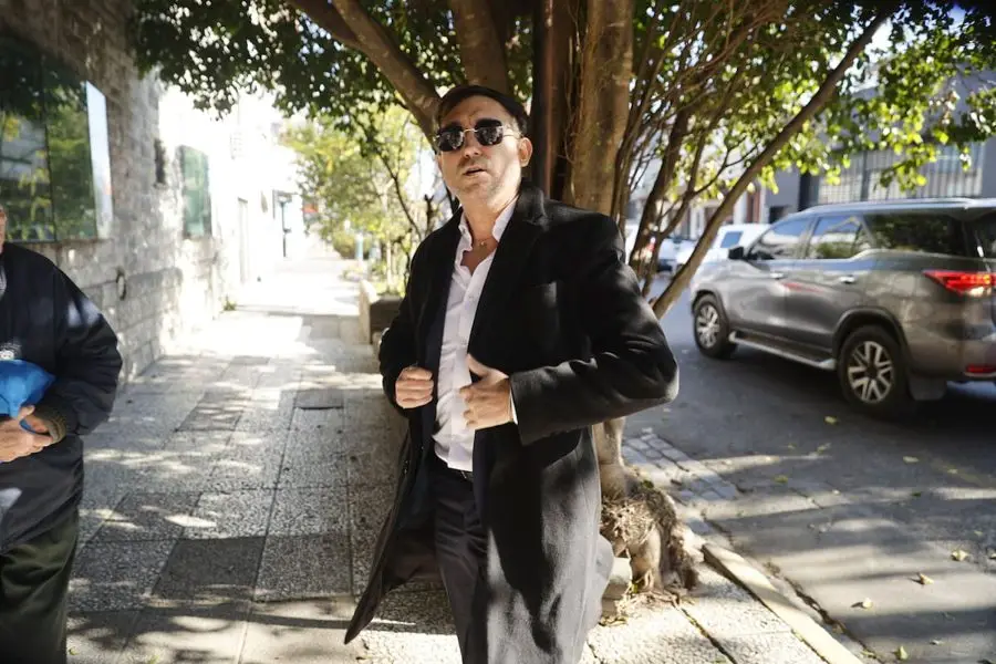 Ariel Vallejo, de saco negro y anteojos oscuros, camina por una vereda arbolada. Foto: La Nación