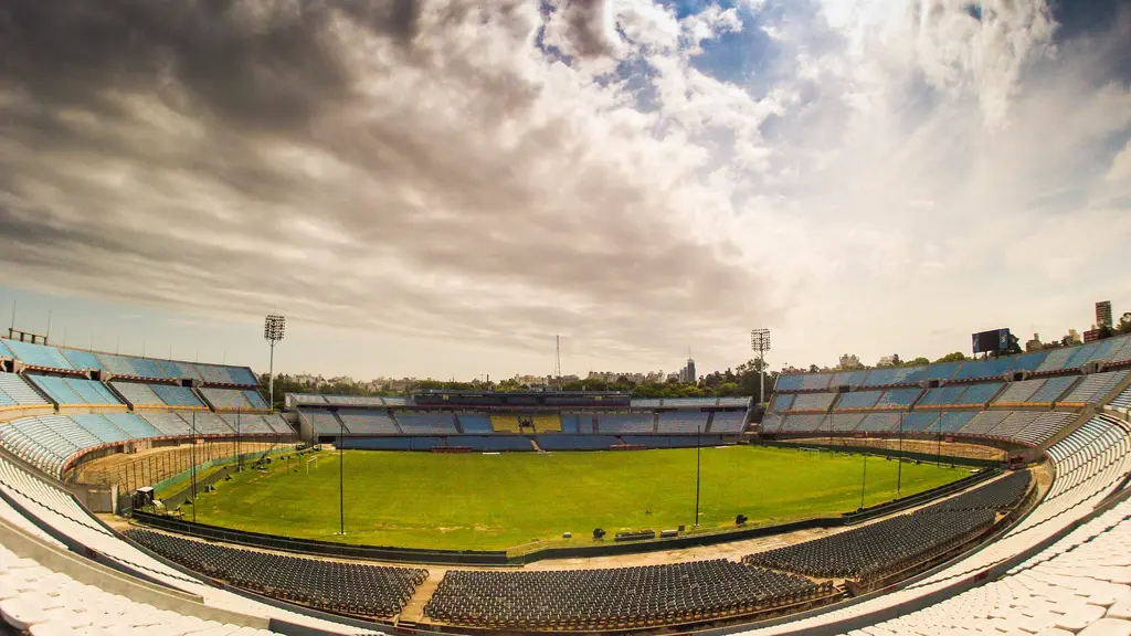 Vista panorámica del interior del Estadio Centenario vacío, con el campo de juego verde y las tribunas de butacas celestes y blancas bajo un cielo con nubes. Foto: TitiNicola / Wikimedia Commons (CC BY-SA 4.0) (archivo)