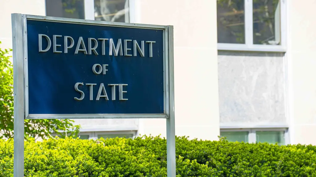 Cartel azul con letras plateadas que dice Department of State frente a la sede del Departamento de Estado en Washington, rodeado de arbustos. Foto: Departamento de Estado de EE.UU. / Wikimedia Commons (dominio público) (archivo)