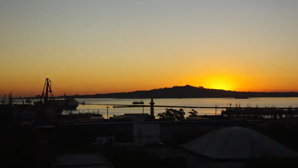 Silueta del Cerro de Montevideo al atardecer, del otro lado de la bahía, con grúas del puerto y techos de la ciudad en primer plano. Foto: Ismael Cordero / Wikimedia Commons (CC BY-SA 3.0) (archivo, imagen ilustrativa)