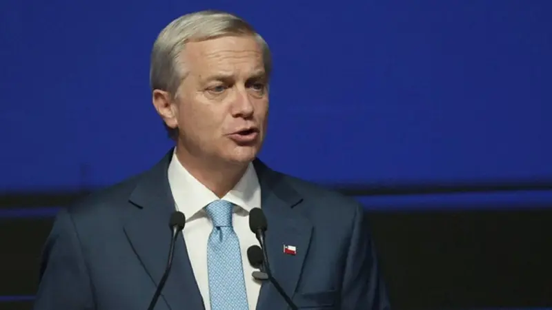 José Antonio Kast habla ante dos micrófonos, con la bandera de Chile en la solapa. Foto: Ámbito