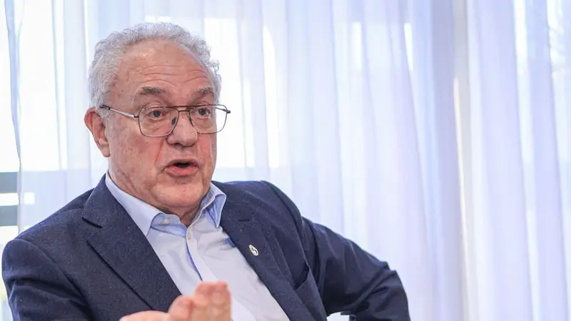 Mario Lubetkin, de anteojos y saco azul, habla sentado frente a un cortinado blanco. Foto: El Observador