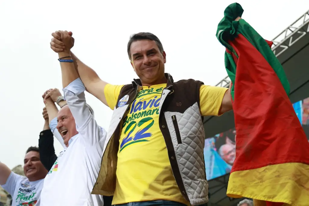 Flávio Bolsonaro, de remera amarilla, levanta los brazos en un acto con una bandera de Rio Grande do Sul. Foto: AFP
