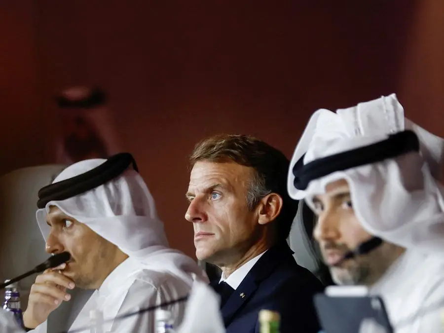 Emmanuel Macron, de traje oscuro, sentado entre dos hombres con keffiyeh blanco durante un acto en Doha. Foto: Clarín
