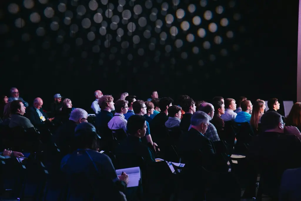 Público sentado en una conferencia, de espaldas al escenario. Foto: Unsplash
