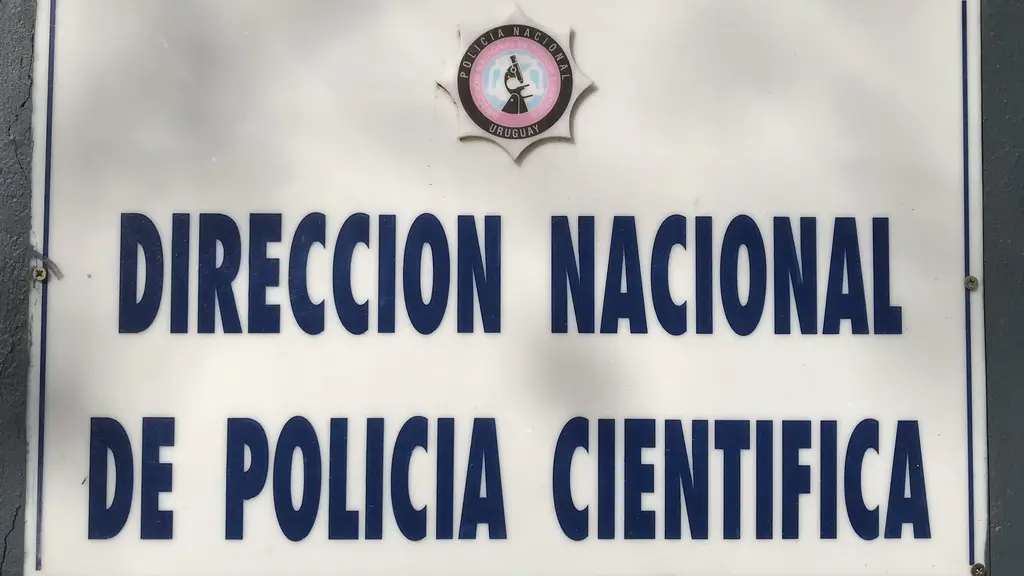Cartel de la DirecciÃ³n Nacional de PolicÃ­a CientÃ­fica con el escudo de la PolicÃ­a Nacional (archivo). Foto: Marinna / Wikimedia Commons (CC BY-SA 4.0)