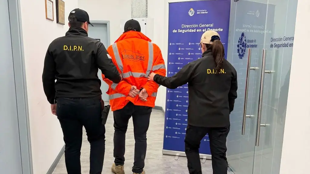 Dos policías de la Dirección General de Seguridad en el Deporte trasladan esposado a uno de los detenidos en la investigación por las amenazas al chofer de UCOT. Foto: Ministerio del Interior