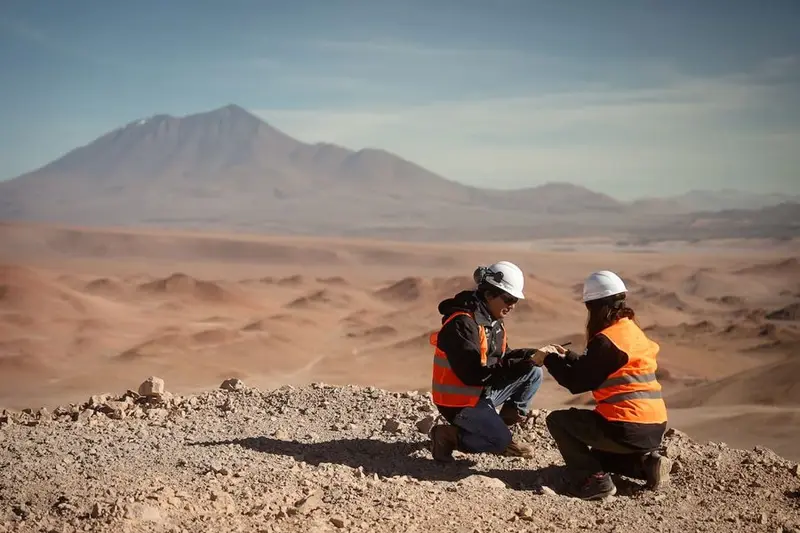 Dos trabajadores con casco y chaleco naranja revisan el terreno en la Puna, con un volcán atrás. Foto: La Nación