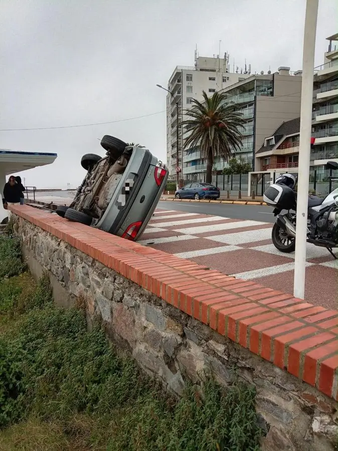 Un auto gris dado vuelta sobre un muro de ladrillos en la rambla de Malvín. Foto: El País