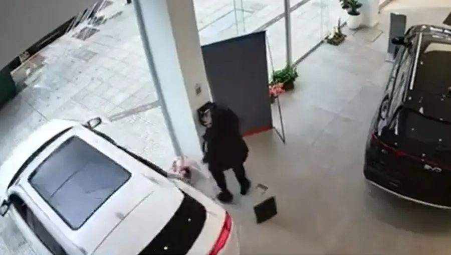 Un auto blanco atraviesa la vidriera de una automotora mientras una persona se aparta. Foto: El País