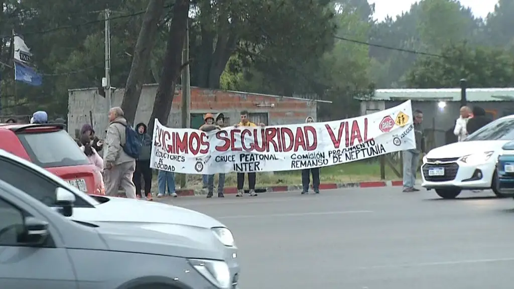 Vecinos sostienen una bandera que pide seguridad vial junto al peaje, con autos pasando. Foto: Subrayado